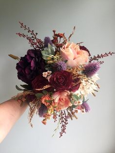 a hand holding a bouquet of flowers on top of a white wall with purple and red colors