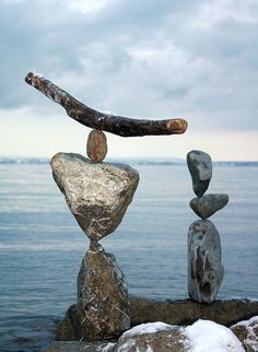 three rocks stacked on top of each other near the ocean with a piece of driftwood sticking out of them