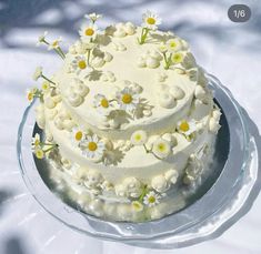 a three layer white cake with daisies on the top and bottom is sitting on a clear plate