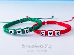 two bracelets with letters and hearts are shown on a white surface, one is green and the other is red