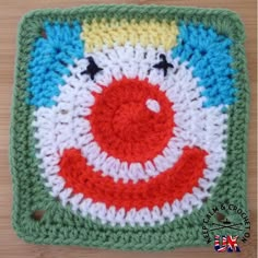 a crocheted square with a smiling clown face on the center and two black dots in the middle