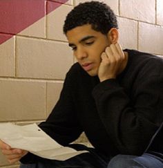 a young man sitting on the floor while talking on a cell phone and holding a piece of paper in his hand