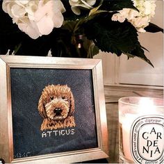 a cross stitch picture frame with a dog's face on it next to a candle and flowers