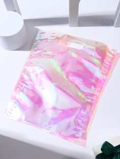 a pink holographic bag sitting on top of a white table next to a roll of toilet paper