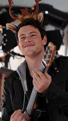 a young man with a deer's head on top of his head holding a guitar