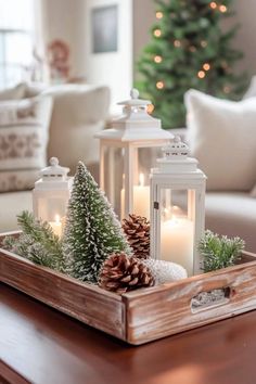 two white lanterns are sitting on a tray with pine cones and evergreens in it