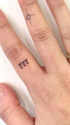 two fingers with small tattoos on them, one has a star and the other has an inscription