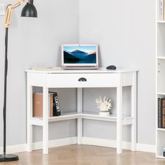 a laptop computer sitting on top of a white desk next to a book shelf and lamp