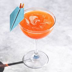 an orange cocktail in a wine glass with a paper airplane sticking out of the top