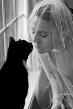 a black and white photo of a woman wearing a veil with a cat in front of her