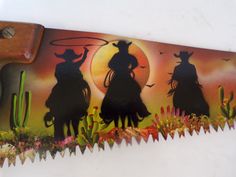 a cowboy themed belt buckle with three silhouettes on horses in front of a sunset