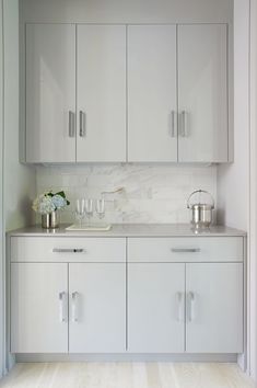 a kitchen with white cupboards and marble counter tops on the wall, along with two vases filled with flowers