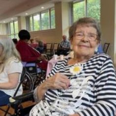 an elderly woman sitting in a chair with other people around her and smiling at the camera