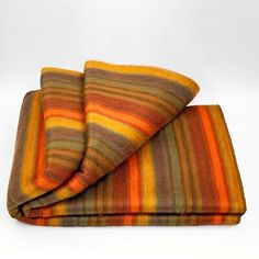 an orange, yellow and brown striped blanket folded on top of each other in front of a white background