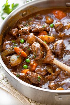 beef stew with carrots, potatoes and parsley in a large metal pot on a white cloth