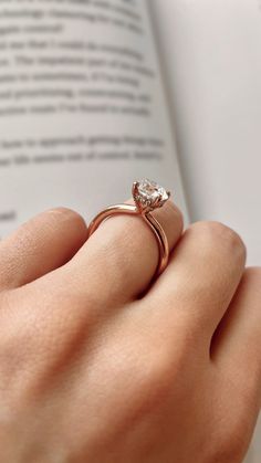 a woman's hand with a ring on it and an open book in the background