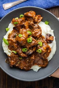 a plate filled with meat and potatoes covered in gravy on top of mashed potatoes