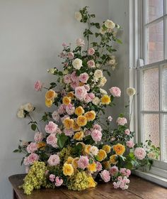 a bunch of flowers that are on top of a wooden table in front of a window