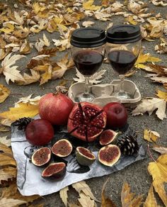 two glasses of wine and some fruit on the ground with leaves around them in fall