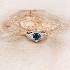 an engagement ring with a green stone in the center on top of a piece of wood