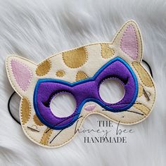 a cat mask with purple and gold details on the front, sitting on a white fur surface