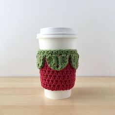 a crocheted coffee cup cozying with a green leaf on the top and red bottom