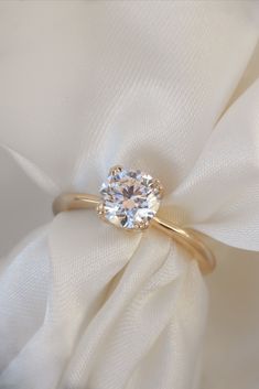 a close up view of a diamond ring on a white cloth with a flower in the background