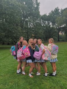 four girls are standing in the grass with backpacks on their backs and one girl is holding onto her back