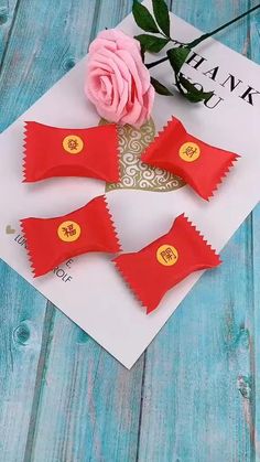 two red candy bows with gold buttons on them and a pink rose next to it