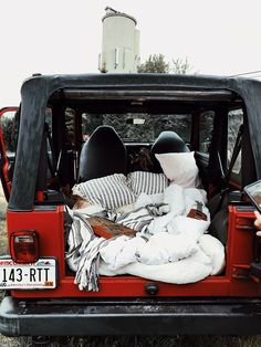 the back end of a red truck with blankets and pillows in it's bed