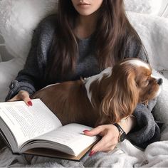 a woman is reading a book with her dog