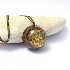 a necklace with a flower of life pendant on it sitting next to a white rock