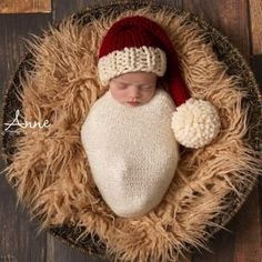 a newborn baby wearing a santa hat and sleeping in a basket on a wooden floor