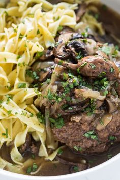 a white bowl filled with pasta and meat covered in mushroom sauce, garnished with parsley