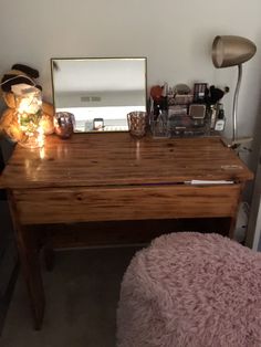 a wooden desk with a mirror on top of it next to a stool and lamp