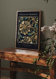 a wooden table topped with a vase filled with flowers next to a framed book cover