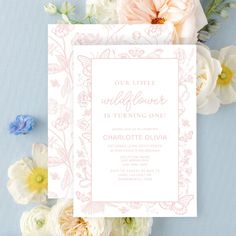 the wedding card is surrounded by flowers and white cards with pink lettering on them, which reads our little wildflower it's turning one