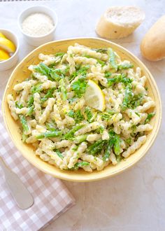 a yellow bowl filled with pasta and broccoli on top of a checkered table cloth