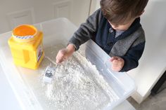 a young boy is playing with flour in his play tray and scooping it into a container