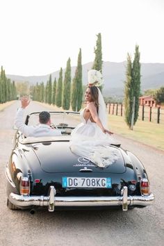 a bride and groom in an old black convertible car on the side of a road