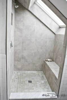 a walk in shower sitting next to a white tiled wall and floor under a slanted skylight