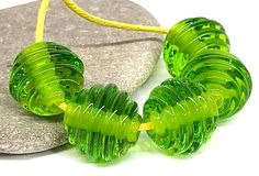 three green glass beads sitting on top of a rock next to a yellow cord and stone