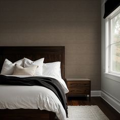 a bed with pillows and blankets in a bedroom next to a window on a wooden floor