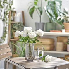 some white roses are in a vase on a small table with water and two glasses