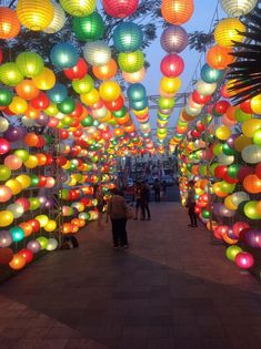 many colorful lanterns are hanging from the ceiling in an open area with people walking underneath them