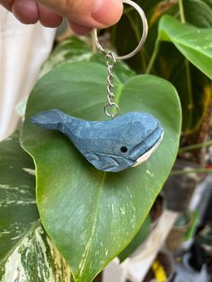 a blue bird keychain sitting on top of a green leafy plant next to a hand