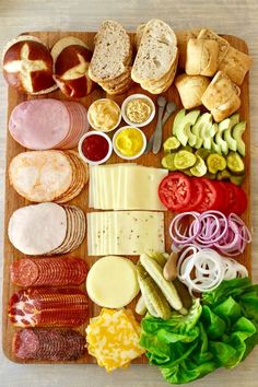 an assortment of meats, cheese and vegetables on a cutting board with bread slices