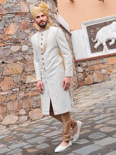 a man in a white outfit standing on a cobblestone street next to a stone wall