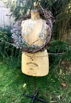 an old mannequin is adorned with twigs and lavenders in a garden area