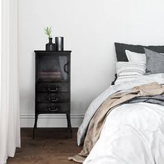 a bedroom with white walls and wooden flooring, a black nightstand stands next to the bed